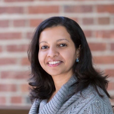 Woman with dark hair smiles in front of a brick wall
