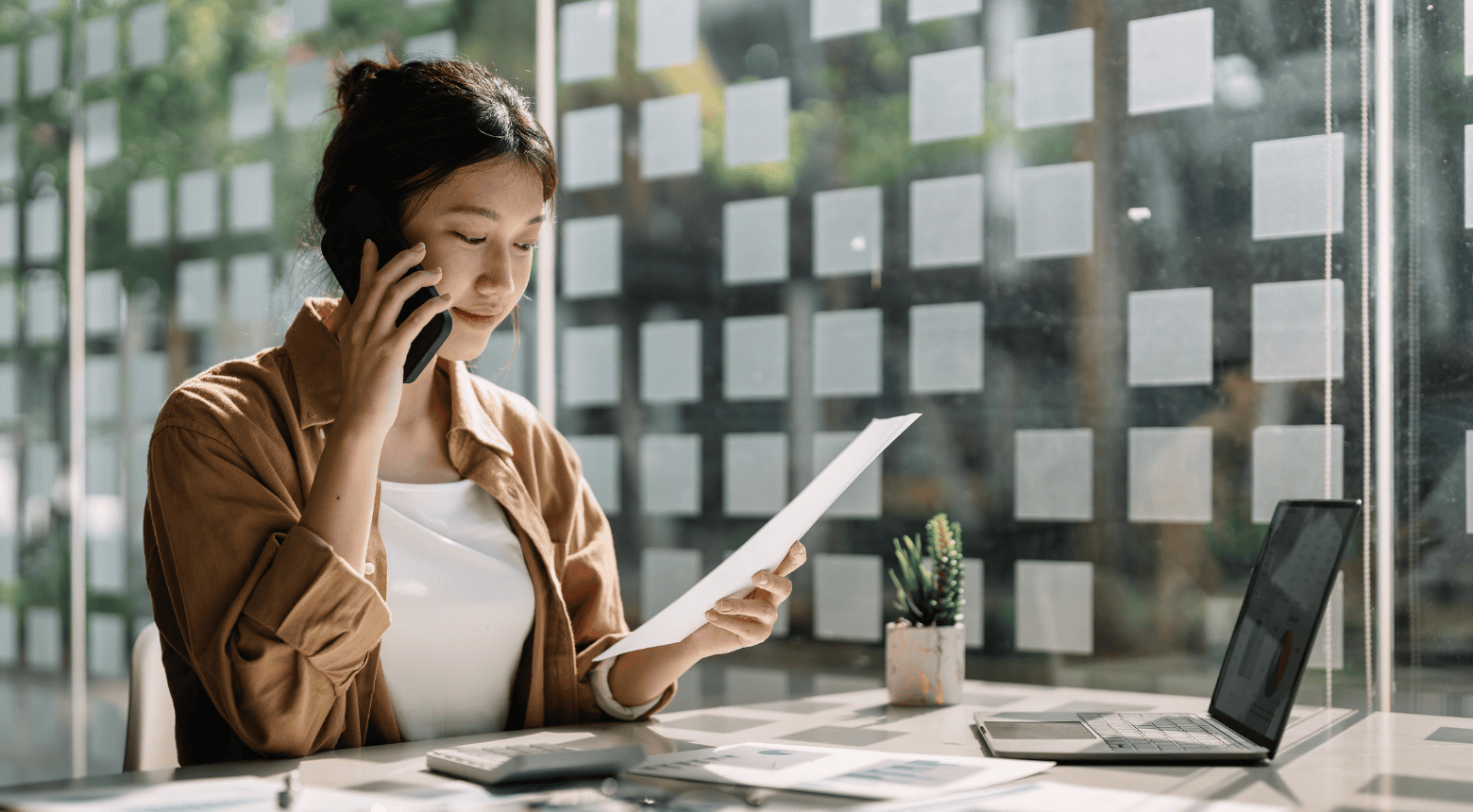 Woman on phone reviewing document at desk, possibly consulting
